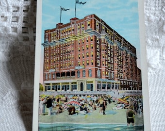 May include: Vintage postcard featuring a red brick building with the text "Hotel Knickerbocker, Boardwalk at Tennessee Avenue, Atlantic City, N. J.". The building is located on a beach with people in bathing suits.