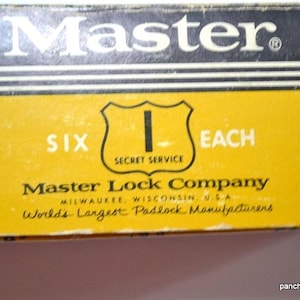 May include: Close-up of a yellow and black box with the word "Master" in white. The box has the text "SIX EACH" and "SECRET SERVICE". The Master Lock Company is also printed on the box.