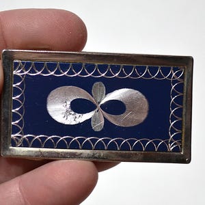 Peut inclure: Pince à billets rectangulaire argentée avec un centre en émail bleu foncé. Le centre présente un motif de symbole infini argenté. Les bords sont décorés d'un motif festonné. Un accessoire vintage.