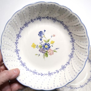 May include: White ceramic bowl with a blue floral design. The bowl has a scalloped edge with a blue trim and a pattern of small blue dots. A floral bouquet of blue, yellow, and pink flowers is in the center.