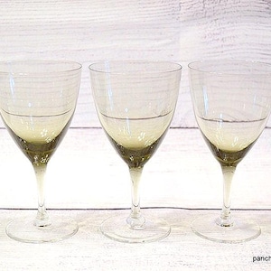 May include: A set of five clear glass stemmed goblets arranged in a row. Each goblet features a distinct ombre effect, transitioning from a dark olive green base at the bottom of the bowl to a completely clear glass rim at the top of the bowl.