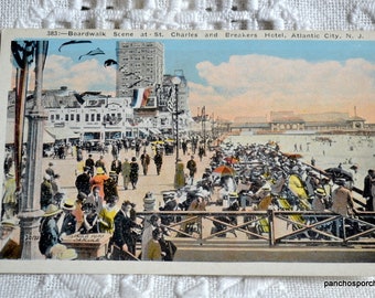 May include: A vintage postcard depicting a bustling boardwalk scene in Atlantic City, New Jersey. The postcard features a view of the St. Charles and Breakers Hotel, with people walking along the boardwalk and enjoying the beach.