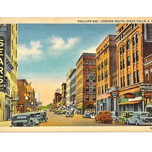 May include: Vintage postcard featuring Phillips Ave. in Sioux Falls, S.D., with the Sears Roebuck & Co. sign. The image shows classic cars and buildings with signs for drugs and a coffee shop. The text reads "PHILLIPS AVE. LOOKING SOUTH, SIOUX FALLS, S. D."