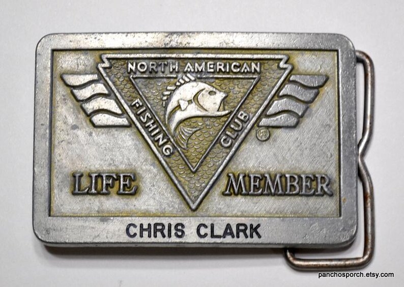 May include: Silver belt buckle with a North American Fishing Club logo featuring a fish and the words "Life Member" and "Chris Clark".