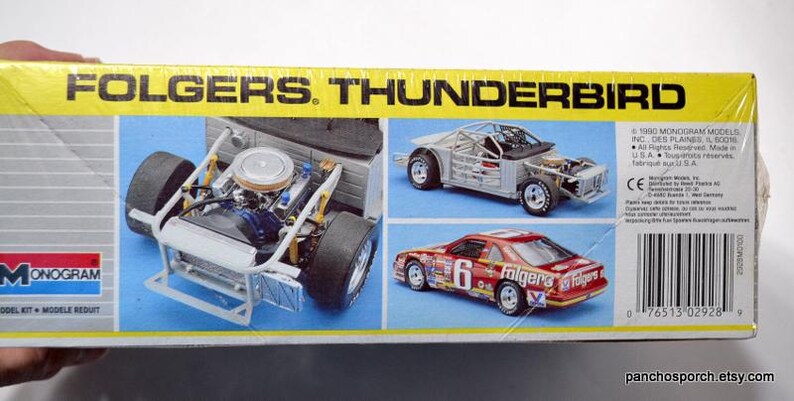 Puede incluir: Caja de modelo de un coche de carreras Folgers Thunderbird. La caja presenta im&aacute;genes del motor, el chasis y el modelo terminado del coche. La caja es amarilla con el texto "FOLGERS. THUNDERBIRD" y el logotipo de Monogram.