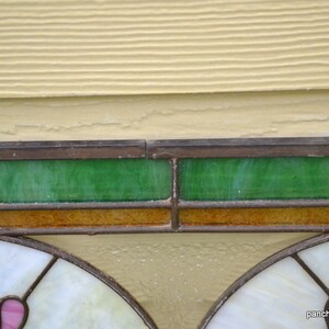 Op de afbeelding: Een glas-in-loodraam met twee panelen met een bloemenmotief. De panelen worden gescheiden door een bruine en groene rand. Het raam is in een houten frame geplaatst.