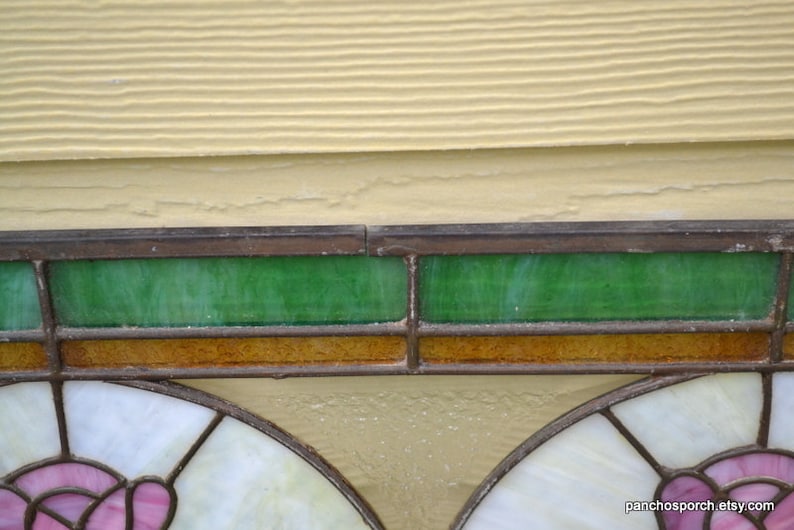 Op de afbeelding: Een glas-in-loodraam met twee panelen met een bloemenmotief. De panelen worden gescheiden door een bruine en groene rand. Het raam is in een houten frame geplaatst.