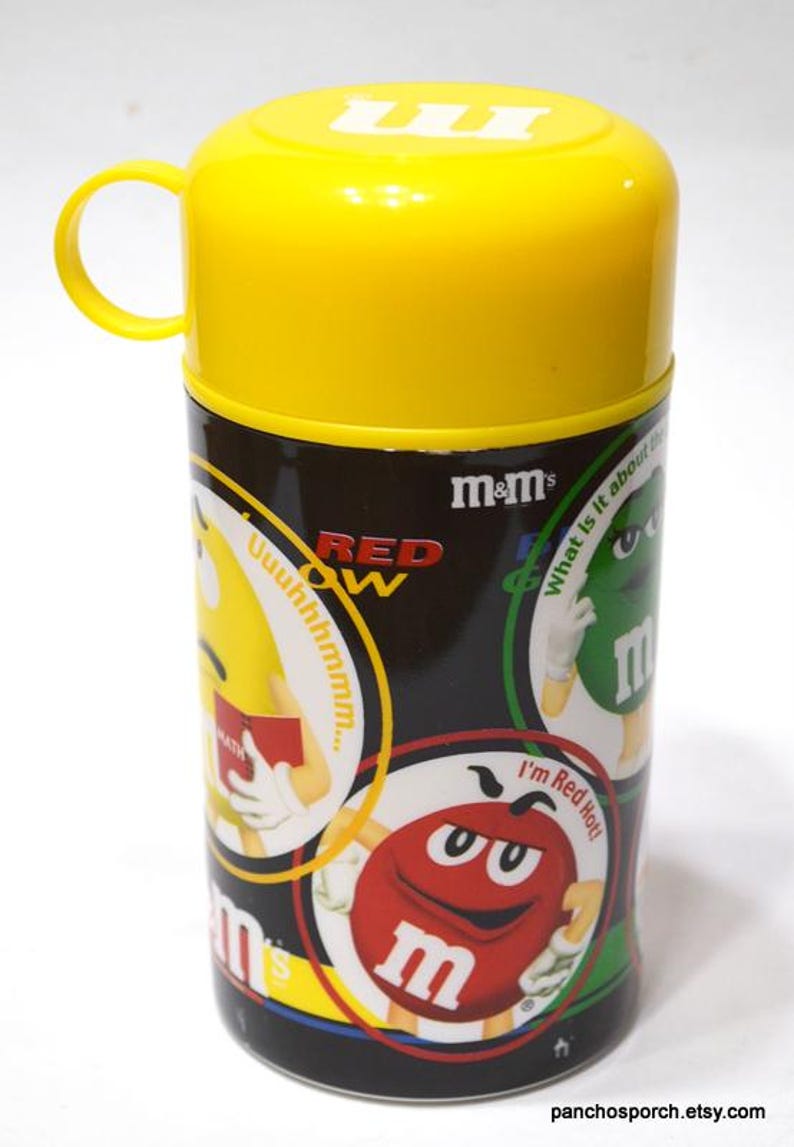 May include: A yellow and black M&M's themed container with a yellow lid and handle. The container features various M&M's characters and the text "RED" and "m&m's". The container is cylindrical.