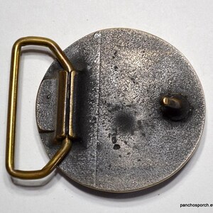 K&ouml;nnte beinhalten: Vintage G&uuml;rtelschnalle aus Metall mit kreisf&ouml;rmigem Design. Die Schnalle hat eine angelaufene silberfarbene Oberfl&auml;che, einen goldfarbenen Rahmen und einen goldfarbenen Verschluss. Die Schnalle ist f&uuml;r einen G&uuml;rtel konzipiert.