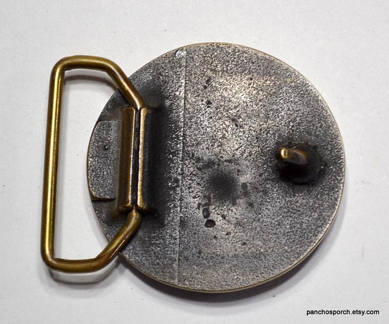 K&ouml;nnte beinhalten: Vintage G&uuml;rtelschnalle aus Metall mit kreisf&ouml;rmigem Design. Die Schnalle hat eine angelaufene silberfarbene Oberfl&auml;che, einen goldfarbenen Rahmen und einen goldfarbenen Verschluss. Die Schnalle ist f&uuml;r einen G&uuml;rtel konzipiert.