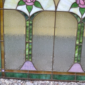 Op de afbeelding: Een glas-in-loodraam met een geometrisch ontwerp met drie roze rozen en groene bladeren. Het raam heeft een matglas effect.