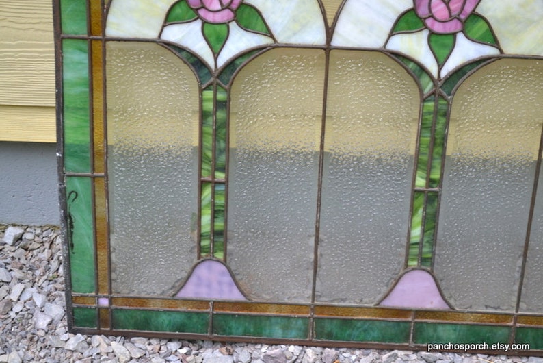 Op de afbeelding: Een glas-in-loodraam met een geometrisch ontwerp met drie roze rozen en groene bladeren. Het raam heeft een matglas effect.