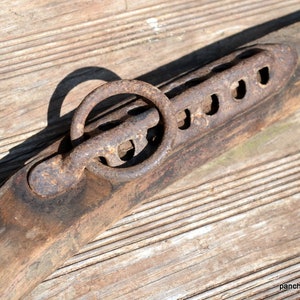 May include: A close-up of a wooden ox yoke with a metal ring and a series of holes. The yoke is weathered and has a rustic appearance.