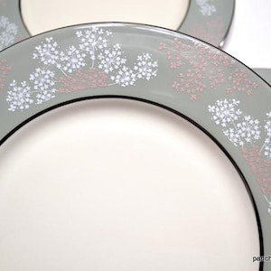 May include: A set of three white ceramic dinner plates with a gray rim and a delicate floral design in white and pink.
