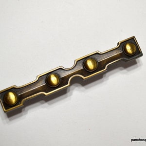 May include: A rectangular, antique brass-toned cabinet pull with four round, gold-colored accents. The hardware has a slightly curved design with a dark, aged finish. The Etsy shop name "panchosporch.etsy.com" is visible in the bottom right corner.