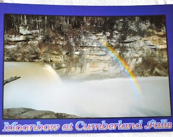 May include: A postcard featuring a photograph of a rainbow over a waterfall. The text "Moonbow at Cumberland Falls" is printed at the bottom of the postcard.