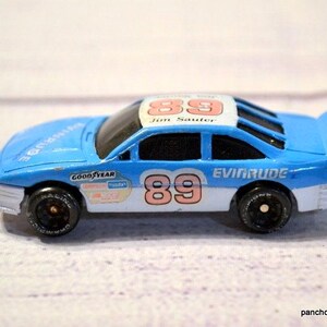 May include: A blue toy race car with the number 89 on the side and roof. The car has black wheels and the words "Evinrude" and "Goodyear" are visible. The car is a miniature replica of a race car.