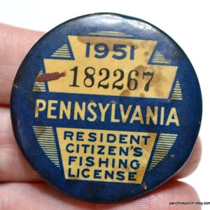 May include: Vintage Pennsylvania Resident Citizen's Fishing License button. The round button is dark blue with yellow text and graphics. The text includes the year 1951 and the license number 182267. The button is slightly worn.