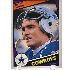 May include: A vintage Topps football card featuring Danny White of the Dallas Cowboys. The card has a portrait of White in his helmet and uniform. The Cowboys logo is visible, along with the Topps logo and the text "QB-P".
