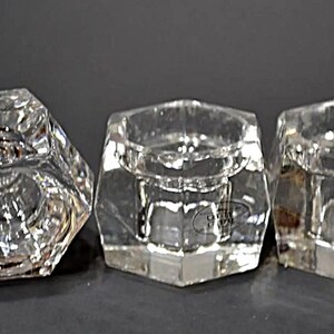 May include: Three clear glass candle holders with a hexagonal shape. The holders have a smooth, polished finish and are designed to hold small candles.
