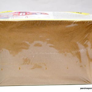 Puede incluir: Una caja rectangular de cart&oacute;n envuelta en pl&aacute;stico transparente. La caja es de color marr&oacute;n claro y parece estar sellada. La parte superior de la caja tiene texto y gr&aacute;ficos visibles.