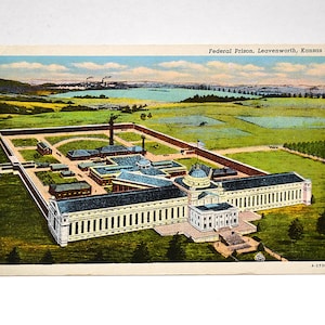 May include: A vintage postcard featuring a colourised illustration of the Federal Prison in Leavenworth, Kansas. The image shows a large complex with a central domed building, long wings, and a surrounding wall, set within a green landscape.