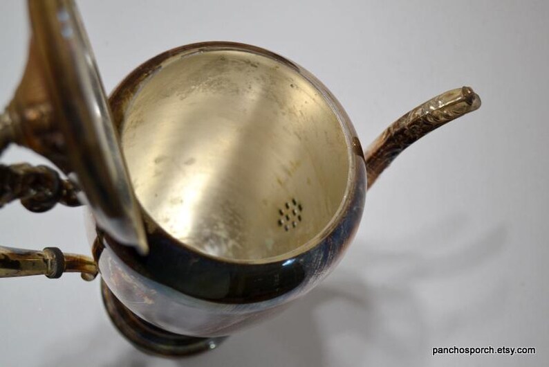 Pu&ograve; includere: Teiera argentata con coperchio e filtro. La teiera ha un design decorativo e un manico.