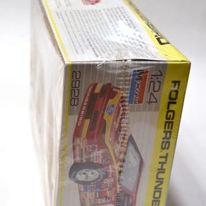 Puede incluir: Una caja de modelo de un coche de carreras Folgers Thunderbird. La caja es amarilla y blanca con una imagen de coche rojo y dorado. La caja est&aacute; envuelta en pl&aacute;stico transparente y tiene el n&uacute;mero 6.