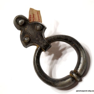 May include: A vintage metal door pull with a decorative ring and a unique design. The pull is in a silver finish and has a worn, rustic look.