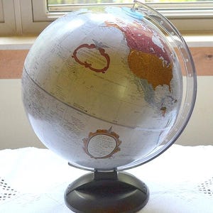 May include: A vintage-style globe with a silver finish, featuring detailed geographical markings and a clear plastic meridian. The globe rests on a black base and has a clear plastic arc. The globe has two labels with text.