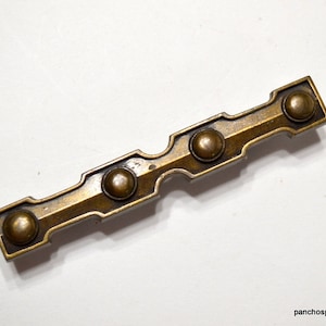May include: A brass drawer pull with a geometric design and four round knobs. The pull is approximately 4 inches long.