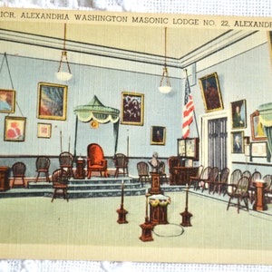 May include: A vintage postcard depicting the interior of the Alexandria Washington Masonic Lodge No. 22 in Alexandria, Virginia. The lodge room features a raised platform with a throne-like chair, surrounded by rows of chairs and a large American flag.