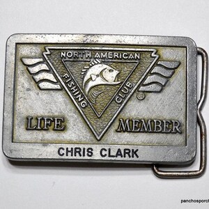 May include: A silver belt buckle with the words "North American Fishing Club" and "Life Member" on it. The buckle also has a fish design and the name "Chris Clark" on it.