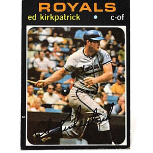 May include: A vintage baseball card featuring Ed Kirkpatrick of the Kansas City Royals. The card has a black border with the word "ROYALS" in orange. The player is in action, wearing a gray uniform.
