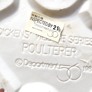 May include: Close-up of a white ceramic piece with embossed text: "DICKENS VILLAGE SERIES POULTERER." A sticker reads "INSPECTED BY 21/8." The piece is marked with "Department 56" and the year 1988.