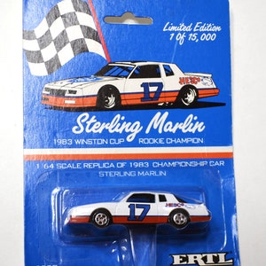 May include: A blue and white carded toy car of the Sterling Marlin 1983 Winston Cup Rookie Champion race car. The car is white with orange and blue accents and the number 17. The card reads "Limited Edition 1 of 15,000".