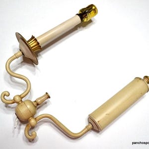 May include: An antique off-white candle-style lamp fixture with brass accents. The fixture has a curved arm and decorative elements. The lamp is designed to resemble a candle and is likely for decorative purposes.