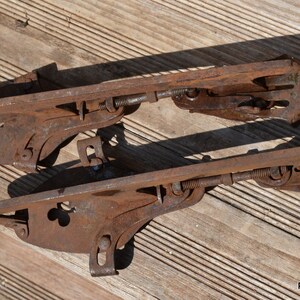 May include: A pair of vintage metal ice skates featuring a rusted brown finish, adjustable screw mechanisms, and clover-shaped cutouts on the side plates. The skates include metal heel and toe clamps for attachment to footwear, with text panchosporch.etsy.com.