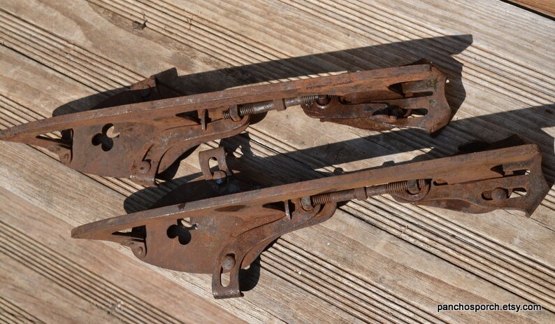 May include: A pair of vintage metal ice skates featuring a rusted brown finish, adjustable screw mechanisms, and clover-shaped cutouts on the side plates. The skates include metal heel and toe clamps for attachment to footwear, with text panchosporch.etsy.com.