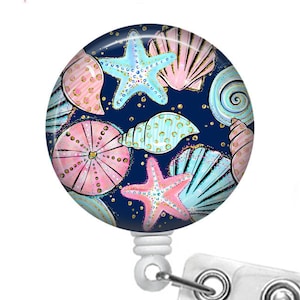 May include: A blue and white seashell themed badge reel with a clear plastic clip. The design features pink, blue, and gold seashells and starfish on a dark blue background.