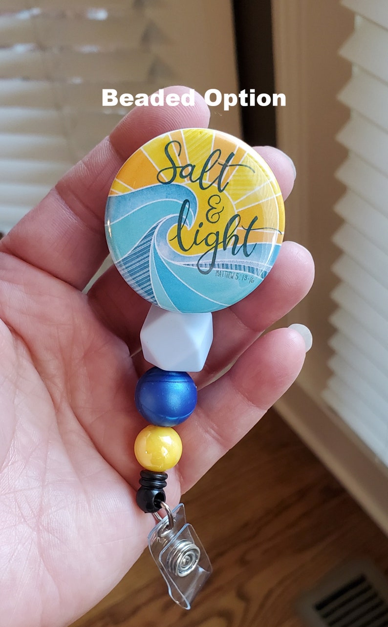 May include: A beaded retractable badge holder with a blue, yellow, and white color scheme. The badge holder features a round button with a wave design and the text "Salt & Light Matthew 5:13-16".