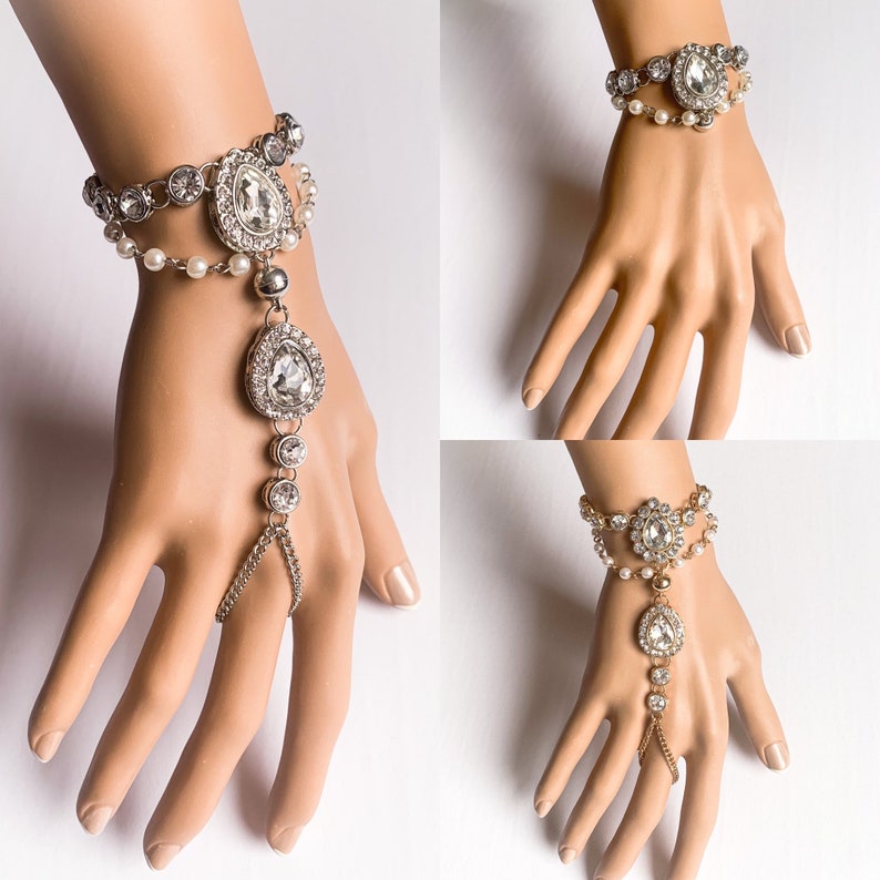 May include: Two silver and gold hand jewelry sets with crystal and pearl accents. The jewelry is a bracelet and a finger ring connected by a chain.