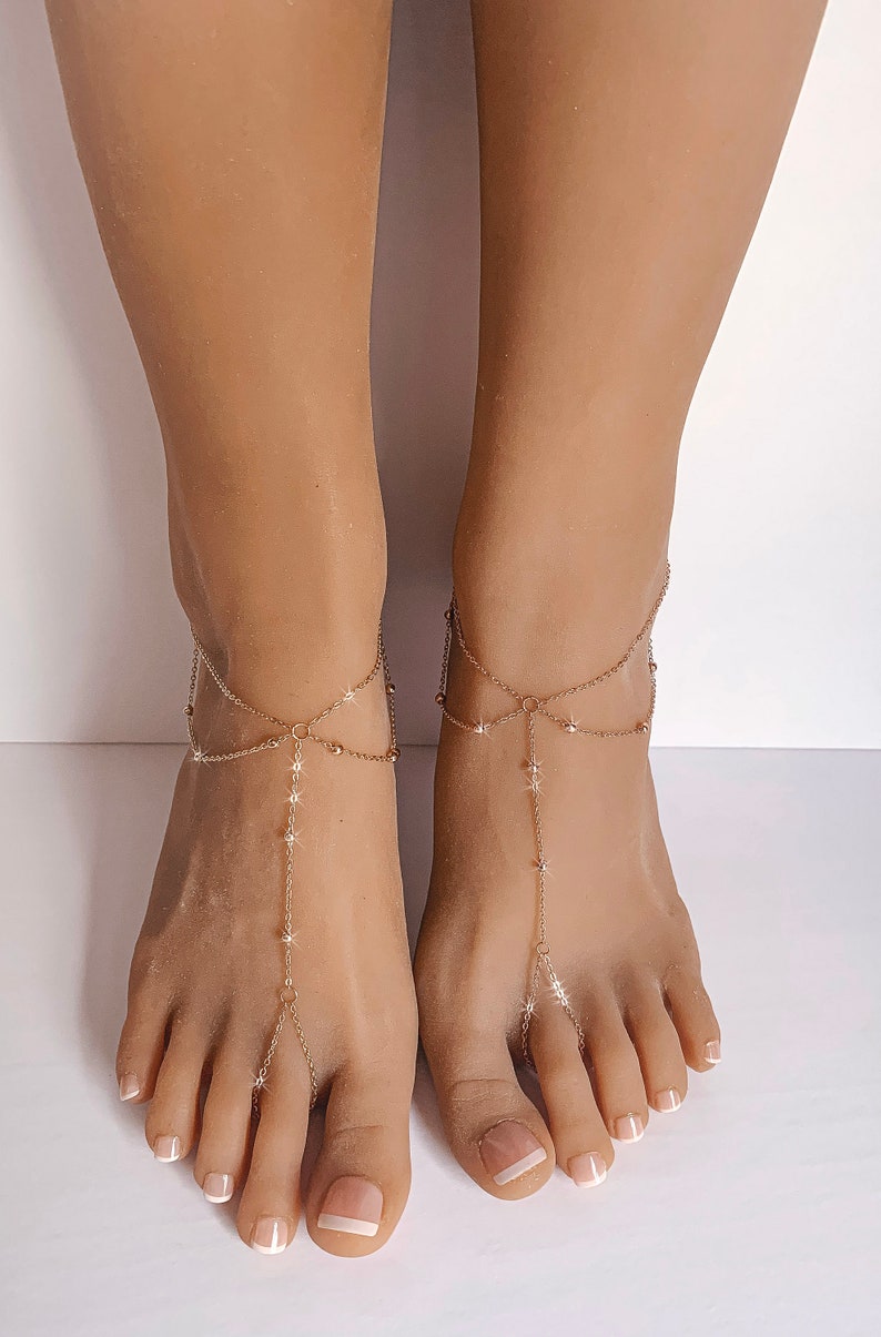 Peut inclure: Sandales pieds nus dor&eacute;es avec des cha&icirc;nes d&eacute;licates et des &eacute;toiles. Les bijoux de pied comportent une cha&icirc;ne qui s'enroule autour de la cheville et se connecte &agrave; l'orteil. Les sandales sont con&ccedil;ues pour &ecirc;tre port&eacute;es sur les pieds.
