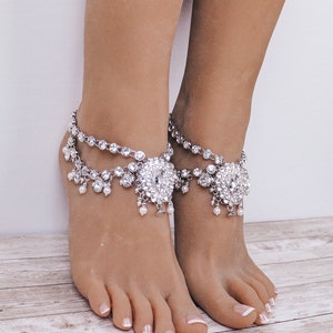 May include: A pair of silver anklets with crystal and pearl embellishments. The anklets feature a large, ornate, crystal-encrusted centerpiece.