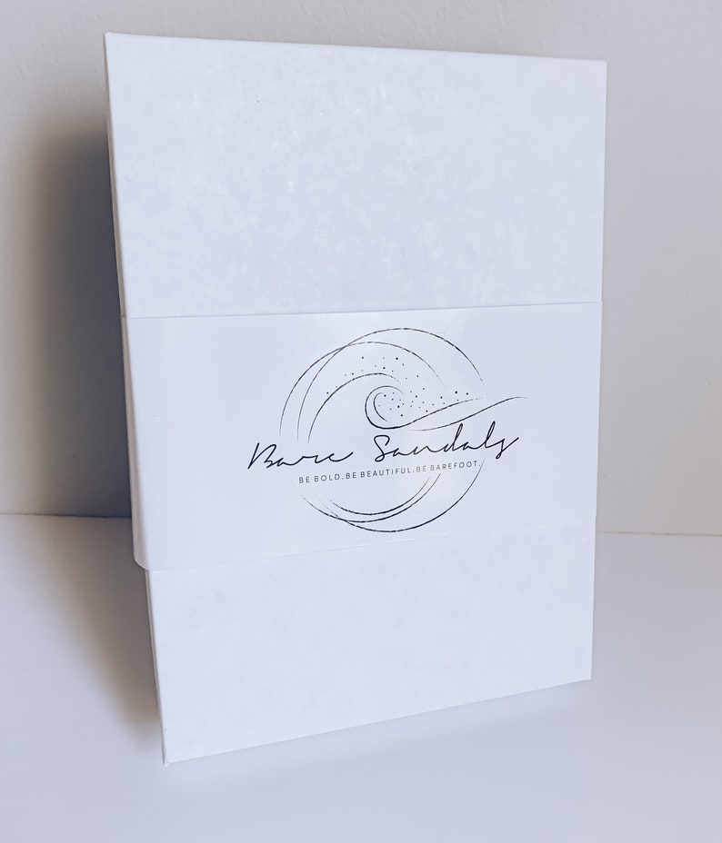 Puede incluir: Caja de cart&oacute;n blanca con un logotipo que dice "Bare Sandals" y el lema "Be bold. Be beautiful. Be barefoot."
