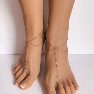Peut inclure: Une paire de bijoux de pied dor&eacute;s, &eacute;galement appel&eacute;s sandales pieds nus, est pr&eacute;sent&eacute;e sur fond blanc. Les cha&icirc;nes d&eacute;licates comportent de petites perles et des accents en forme d'&eacute;toile, avec une boucle pour le gros orteil et une cha&icirc;ne de cheville.