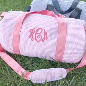 May include: Pink and white striped duffel bag with a pink monogram "KCM" on the front. The bag has a pink strap and a pink and white striped handle.
