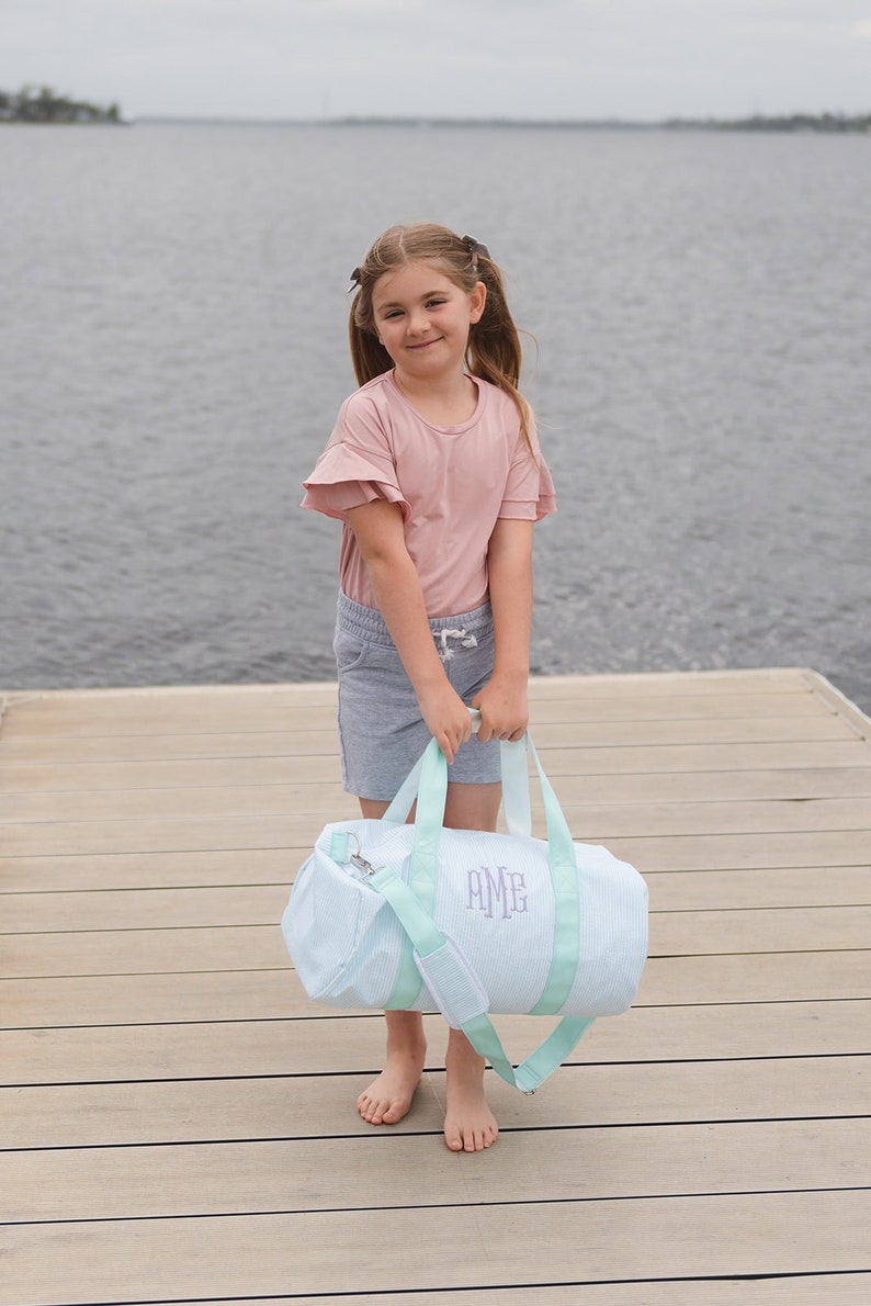 May include: A light blue and white striped duffel bag with a light green trim and a monogram that reads "AME".