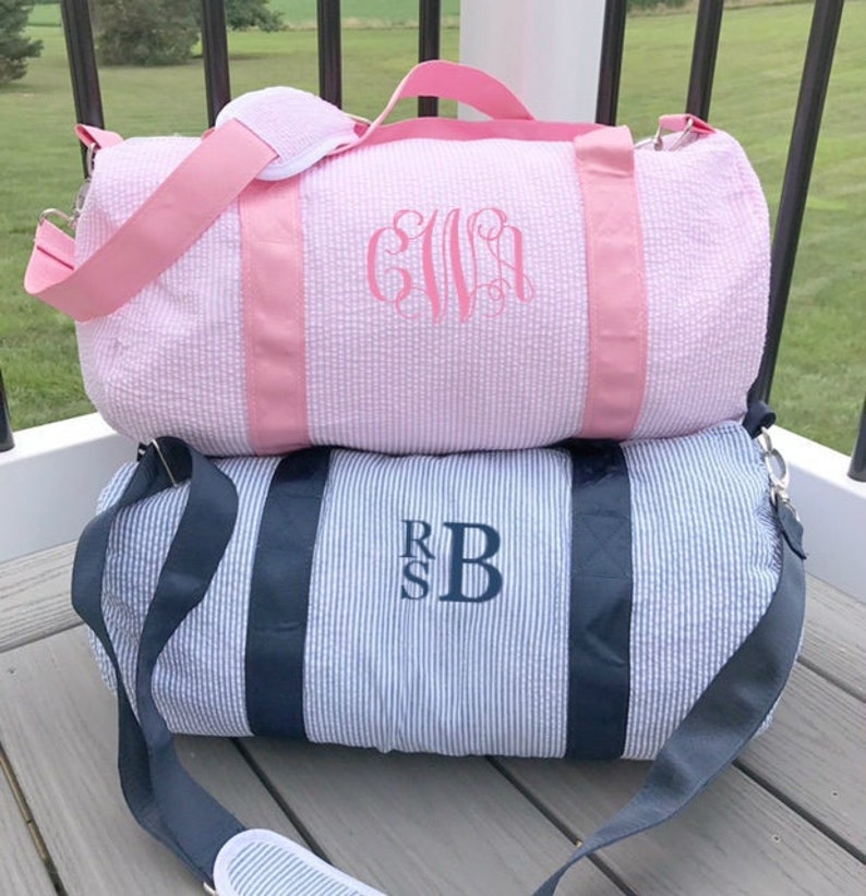 May include: Two monogrammed duffel bags. The top bag is pink with white stripes and the monogram "GIVA". The bottom bag is blue and white striped with the monogram "RSB".