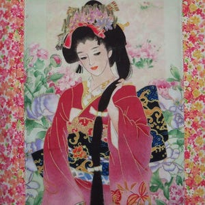 May include: A fabric wall hanging featuring a central illustration of a person with long black hair wearing a red and black kimono with gold accents. The figure is surrounded by pink and purple flowers, framed by a border of small floral patterns.